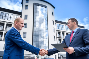 Two businessmen handshaking against new building