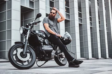 Foto op Plexiglas Pensive handsome bearded biker is relaxing with his bike near interesting building. © Fxquadro