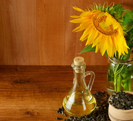 Seeds, oil and sunflowers flower on wooden background. Free space for text.