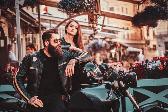 Beautiful couple with brutal biker and his sexy gilfriend are chilling near cefeteria with motorbike.