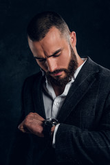 Pensive bearded man in dark suit is checking what time is now at dark photo studio.