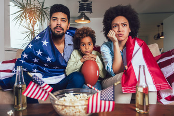 Happy African American family of three watching tv and cheering sport games on sofa at home