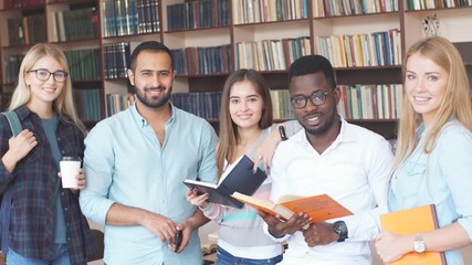 Portrait of multiethnic diverse friends pupils looking at page of interesting book in college library.