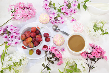 Obraz na płótnie Canvas Colorful pink phlox flowers, cups of coffee, fruits and marshmallows on a light table, top view, flat lay, selective focus. Pink flowers on a light background, a gift for loved ones,