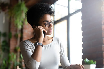 Pensive biracial female busy talking on cellphone at work