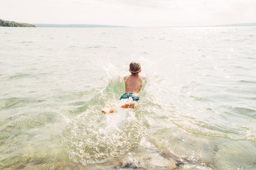 Boy swimming in lake with underwater goggles. Child diving in water with large splash waves. Authentic lifestyle happy childhood. Summer fun outdoor aquatic activity. View from back.