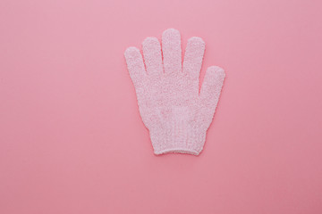 Woman exfoliating massage glove for shower on pink background.Gloves for use in the shower for massage and scrub. Beauty background with cosmetic products. Beauty, health and spa concept