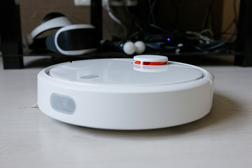 A robot vacuum cleaner removes debris on a laminate. Smart cleaning. White robotic vacuum cleaner.