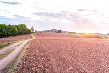 Fototapeta na wymiar Country road in rural agricultural landscape. Red soil fields around Nova Paka, Czech Republic