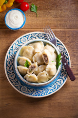 Pierogi or pyrohy, varenyky, vareniki - dumplings in bowl served with sour cream or yogurt on wooden table
