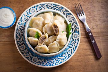 Pierogi or pyrohy, varenyky, vareniki - dumplings in bowl served with sour cream or yogurt on wooden table