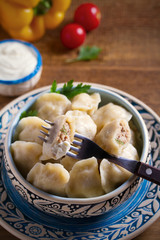 Pierogi or pyrohy, varenyky, vareniki - dumplings in bowl served with sour cream or yogurt on wooden table