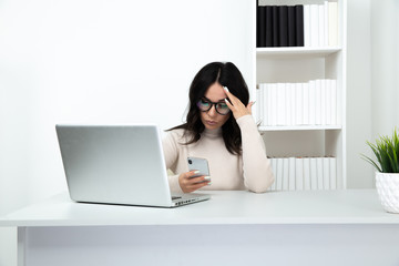 Unhappy and frustrated lady watching phone in office sitting infront of the computer