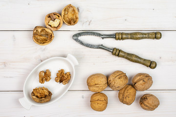Group of lot of whole one half two pieces of ripe brown walnut in white oval ceramic bowl with old nutcracker flatlay on white wood