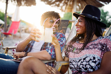 Young happy black couple with drinks relaxing on the beach