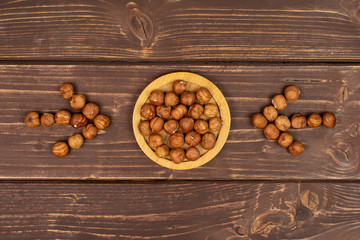 Lot of whole ripe brown hazelnut with arrows on round bamboo coaster flatlay on brown wood