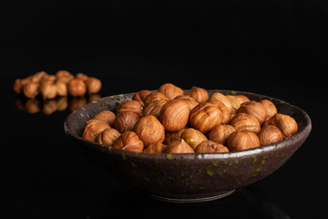 Lot of whole ripe brown hazelnut in dark ceramic bowl isolated on black glass