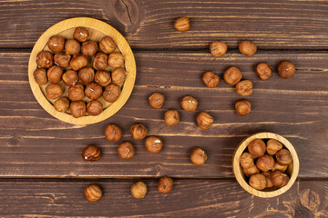 Lot of whole ripe brown hazelnut on round bamboo coaster in tiny wooden bowl flatlay on brown wood