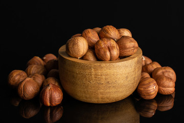 Lot of whole ripe brown hazelnut in tiny wooden bowl isolated on black glass