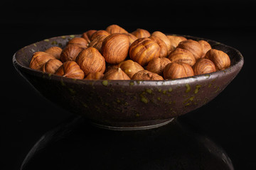 Lot of whole ripe brown hazelnut in dark ceramic bowl isolated on black glass