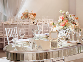 Table served for wedding banquet with cutlery and flowers in vases. Pastel colored decorations.