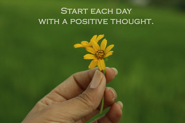 Inspirational quote - Start each day with a positive thought. Beauty in hand concept. Yellow flower in hand. Young woman fingers holds little daisy flowers.