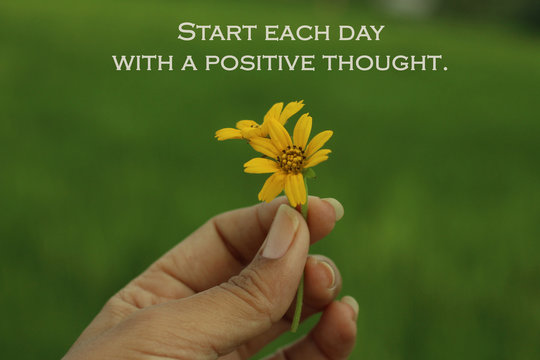 Inspirational quote - Start each day with a positive thought. Beauty in hand concept. Yellow flower in hand. Young woman fingers holds little daisy flowers.