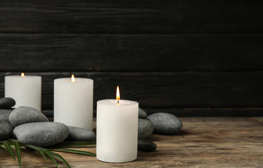 Fototapeta na wymiar Burning candles, spa stones and palm leaf on wooden table, space for text