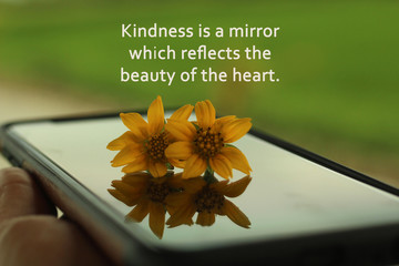 Inspirational quote - Kindness is a mirror which reflects the beauty of the heart. With two daisy flowers on device surface. Kindness and mirror reflections concept. 