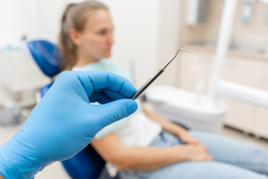 Close-up hand of dentist in the glove holds tool probe and mirror. The patient in the dental chair at the background. Dental work in clinic. Office where dentist conducts inspection and concludes.