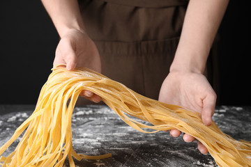 Woman holding raw egg noodles over grey table, closeup