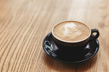 Cup of cappuccino with latte art on wooden background. Black ceramic cup, place for text.