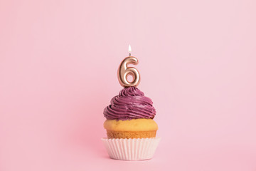 Birthday cupcake with number six candle on pink background