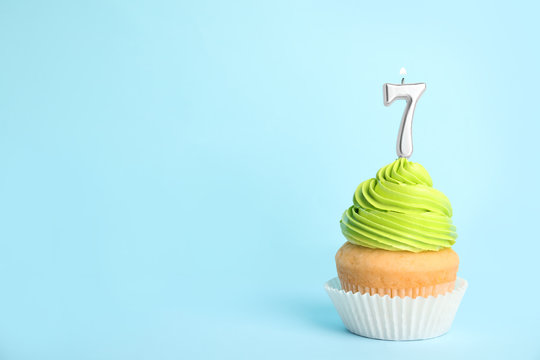 Birthday cupcake with number seven candle on blue background, space for text