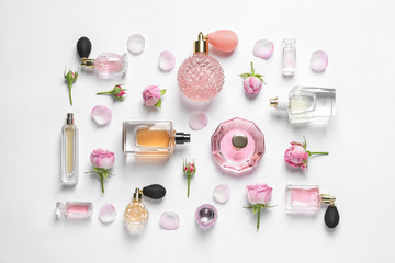 Different perfume bottles and flowers on white background, top view
