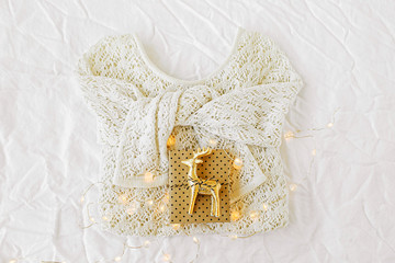 Knitted white sweater and christmas gift with mini golden deer on white background. Winter fashion concept. Top view flat lay.