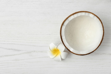 Half of coconut and flower on white wooden background, top view. Space for text