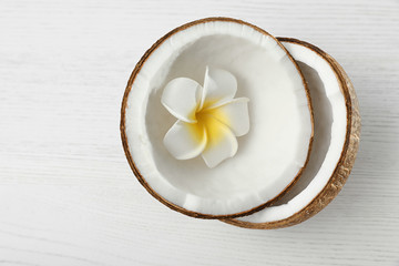 Obraz na płótnie Canvas Halves of coconut and flower on white wooden background