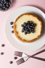 Plate with delicious cheesecake and two forks on pink background.