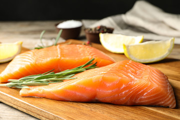 Wooden board with salmon fillet on table, closeup