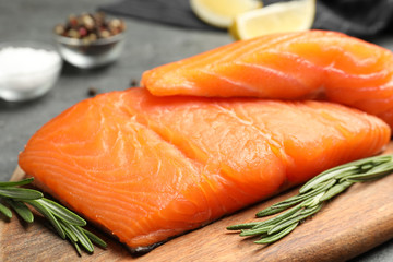 Wooden board with salmon fillet on grey table, closeup