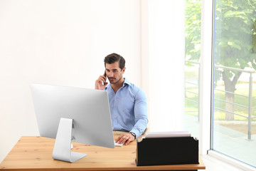 Handsome young man working with smartphone and computer at table in office