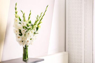 Vase with beautiful white gladiolus flowers on wooden table near color wall. Space for text