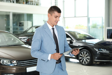 Young salesman with clipboard in modern car dealership