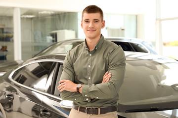 Young man near new car in modern auto dealership
