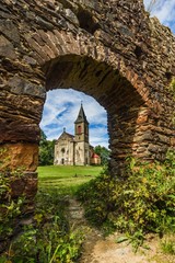 Obraz premium Krasikov, Kokasice / Czech Republic - August 9 2019: View of the old church of Mary Magdalena through a door in a stone wall of Svamberk castle. Sunny summer day. Vertical image.