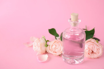 Obraz na płótnie Canvas Bottle of essential oil and roses on pink background