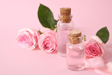 Obraz na płótnie Canvas Bottles of essential oil and roses on pink background