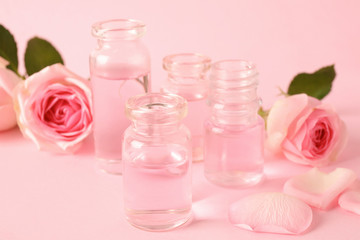 Bottles of essential oil and roses on pink background