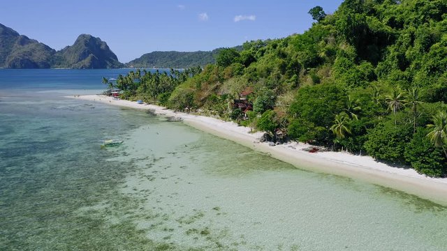 4k Aerial drone circle fly around tropical sandy beach with local boats in shallow water and coconut palm trees. El Nido. Palawan, Philippines